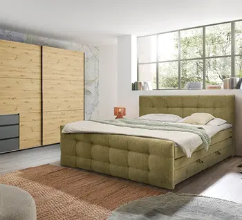 Grünes Polsterbett mit Kleiderschrank aus Holz im hellen Schlafzimmer.